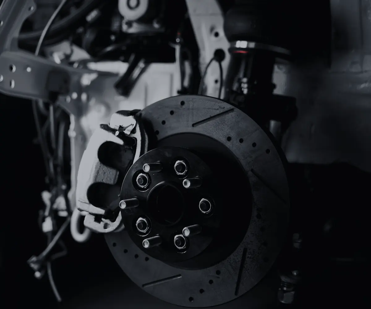 Close up of a drilled and slotted brake rotor, caliper and hub